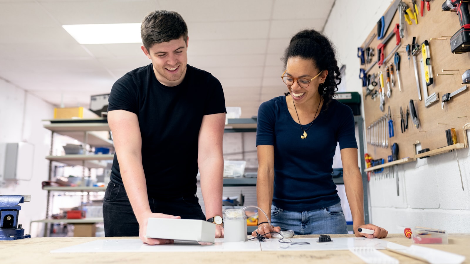 two people working on something together at a workbench, tools on the wall behind them