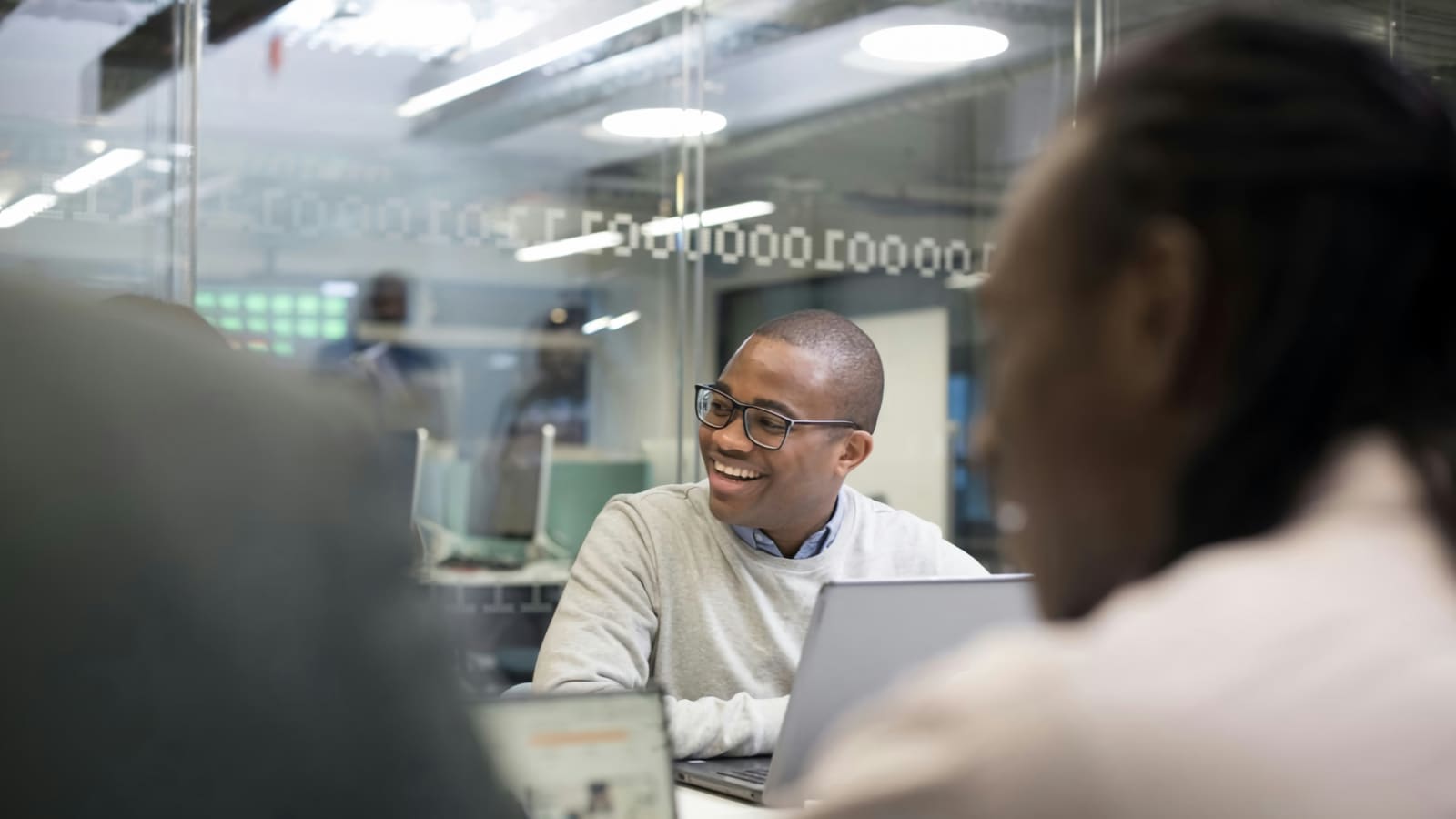 two colleagues talking over laptops in a bright office