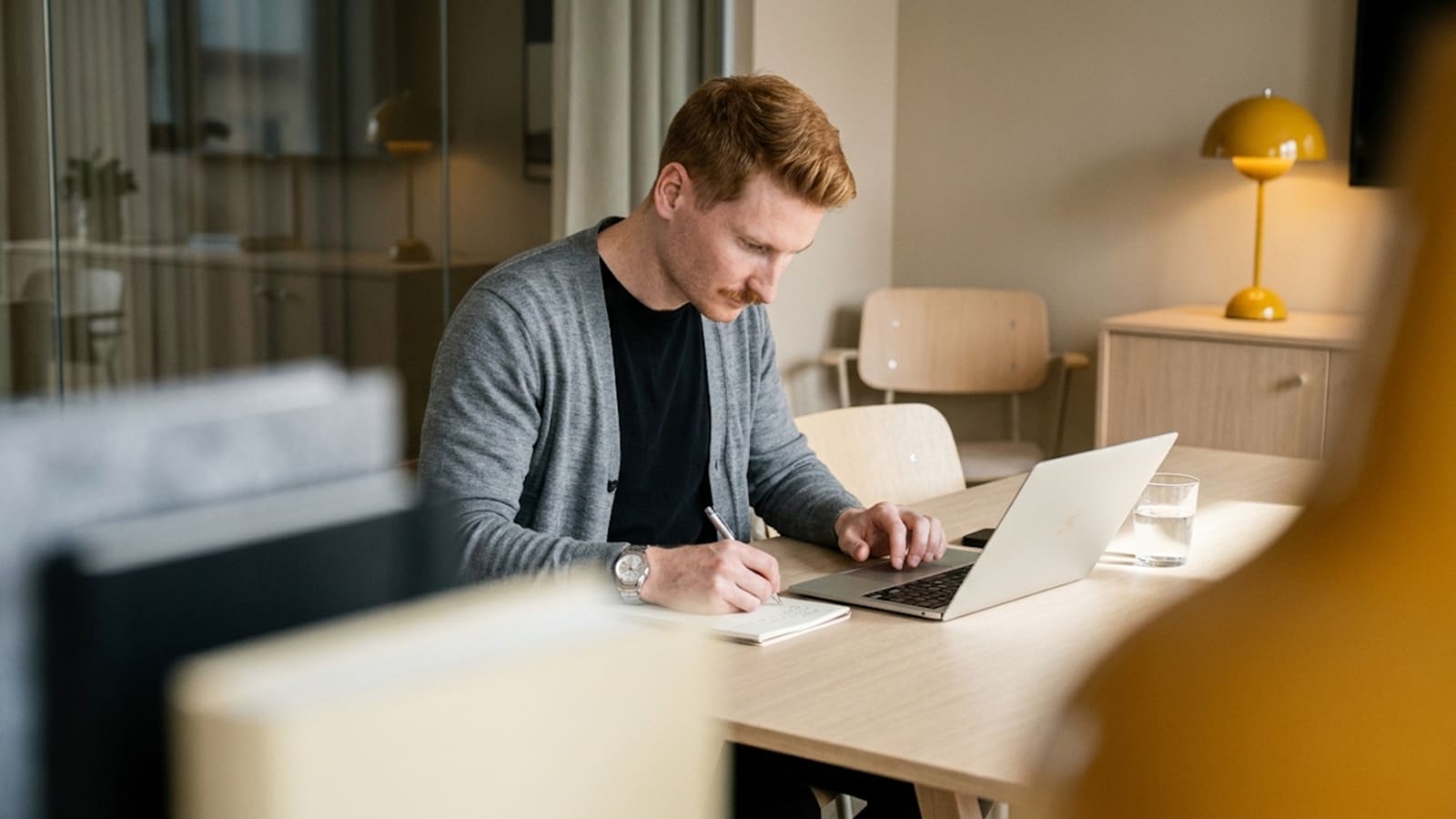somebody writing by hand beside a laptop