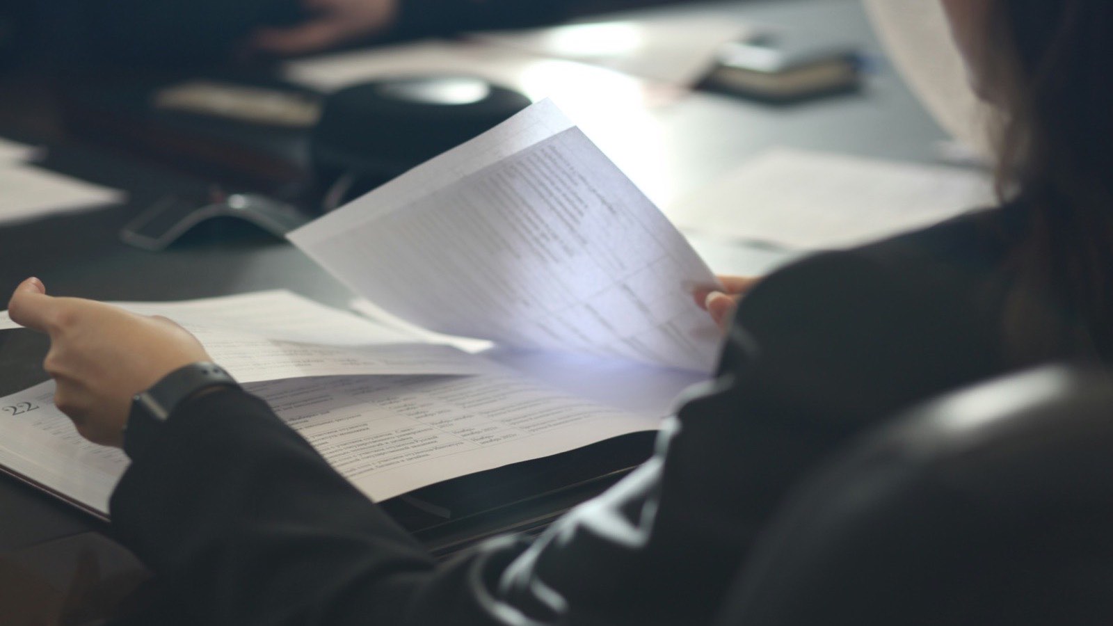 somebody turning the pages of a printed document at a meeting table