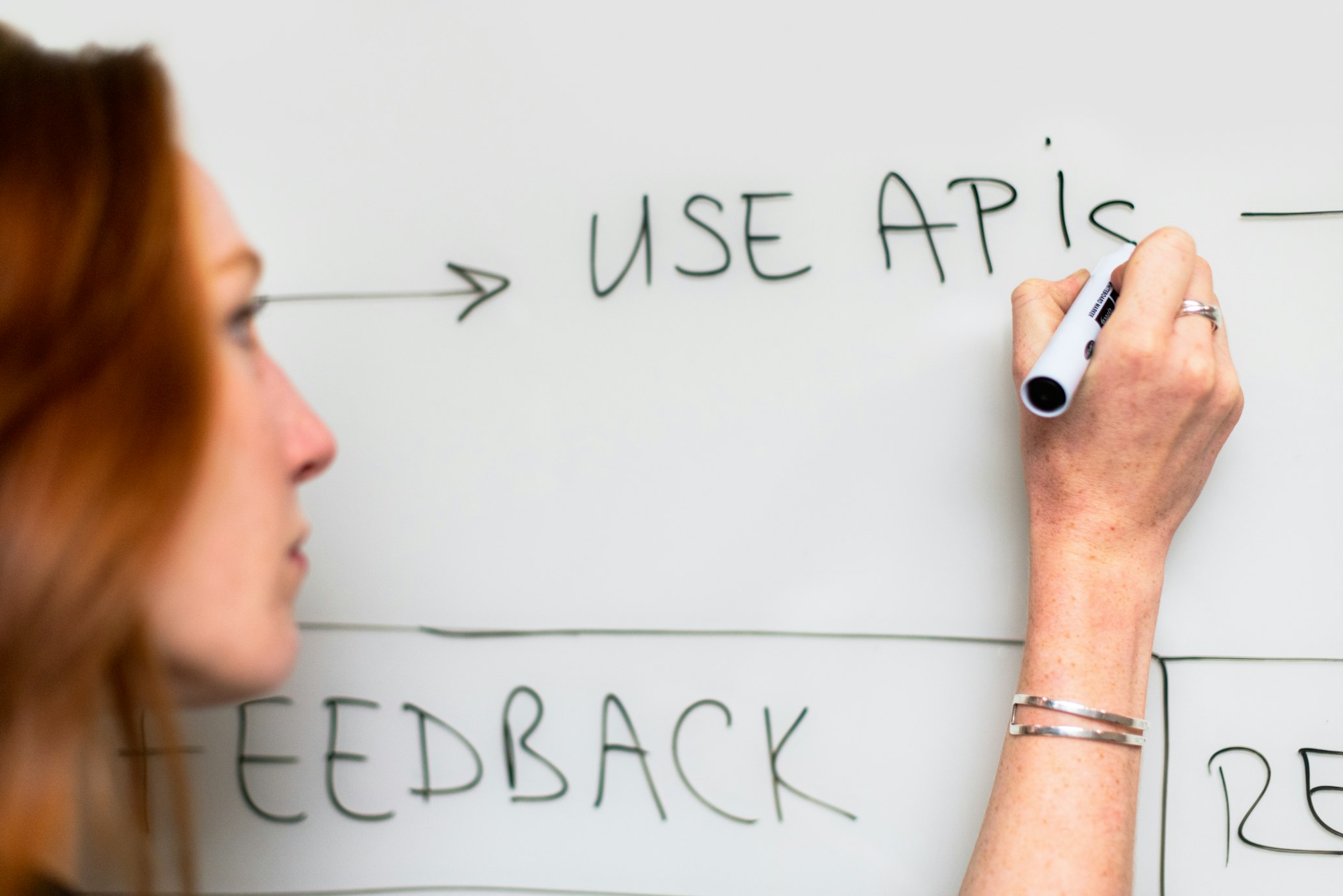 somebody writing "use APIs" on a whiteboard, another person's profile blurred in the foreground